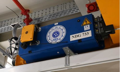 Blauer GKD-Seilzug NDG 733 an gelbem Träger montiert, mit Warnsymbolen und CE-Kennzeichnung in Hallendecke.