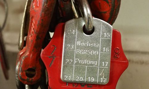 Prüfplakette mit „Nächste BGR500 Prüfung“ an rotem Kranhaken mit Jahreszahlen.